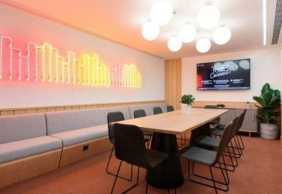 Modern meeting room featuring a light wood table, black chairs, and a colorful neon wall installation.
