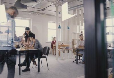 Open plan office space with people working at black desks viewed through a glass partition.