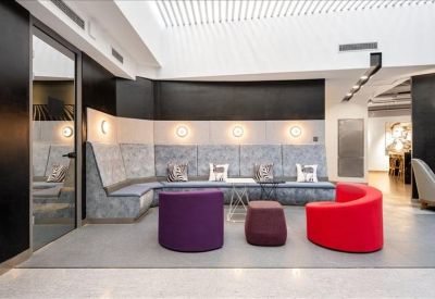 Communal lounge area featuring a grey curved sofa and vibrant purple and red ottomans.