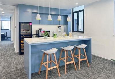 Sleek office pantry with a blue breakfast bar, three wooden stools, and modern coffee facilities.