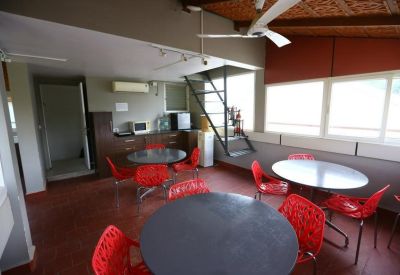 Communal dining area with round tables and vibrant red chairs.