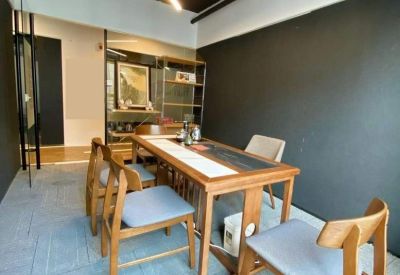 Casual meeting area with a long wooden table, grey chairs, and a triangular feature light.