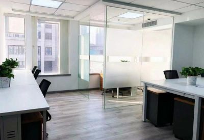 Open-plan office space featuring white desks, potted plants, and glass dividers.