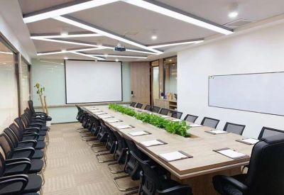Large professional boardroom with a long wooden table, green plants, and a presentation screen.