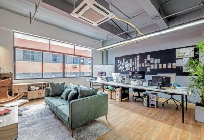 Open-plan office with a green velvet sofa and long workstations under industrial ceilings.