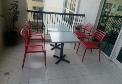 Outdoor balcony seating area with a table and four red chairs overlooking the city.