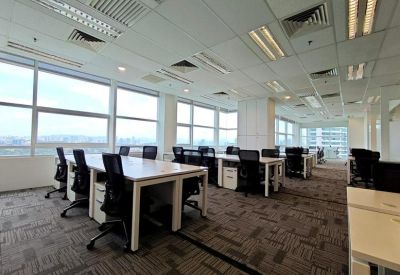 Bright open-plan office with rows of white desks and large windows.