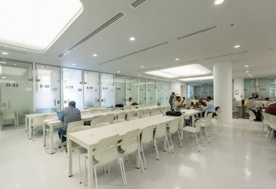 Spacious open-plan workspace with long white desks and glass-partitioned private offices.