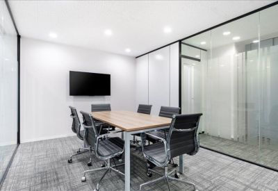 Modern conference room with a wood-finish table, black mesh chairs, and glass partition walls.