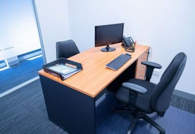 Private office suite with a wooden desk, computer setup, and blue carpet.
