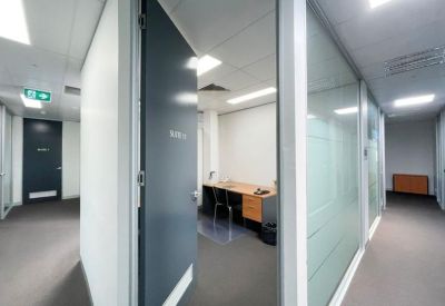Bright, white office corridor showing a private office suite with a desk and chairs.