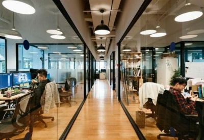 Glass-walled corridor looking into modern private office suites with natural wood flooring.