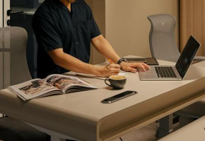 Worker using a standing desk in an office with a laptop and coffee.