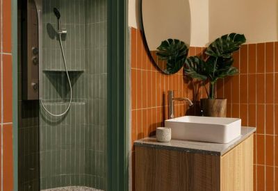 Modern bathroom with orange vertical tiles, a wooden vanity, and a green tiled shower.