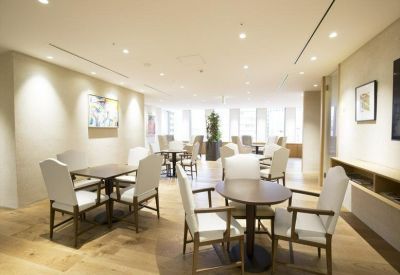Bright communal lounge with wood flooring and several round cafe tables and white armchairs.