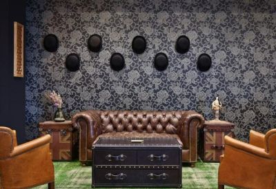 Lounge area with a leather Chesterfield sofa and bowler hats on patterned wallpaper.