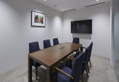 Professional meeting room with a wooden table, navy blue chairs, and a wall-mounted screen.