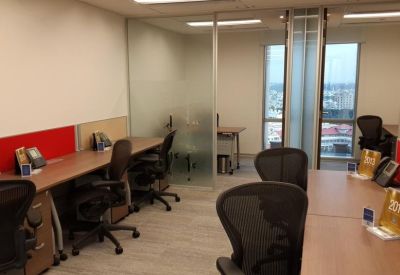 Bright open-plan office with multiple workstations, ergonomic chairs, and a glass-partitioned private room.