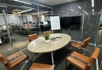 Small meeting room with an oval wooden table, tan leather chairs, and a presentation screen.