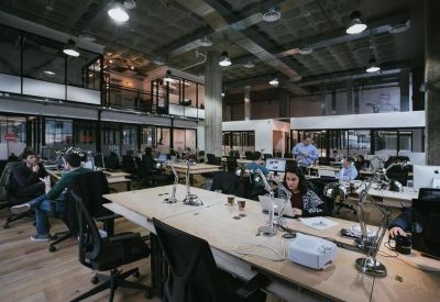 Large open-plan office with long wooden desks and industrial ceiling.