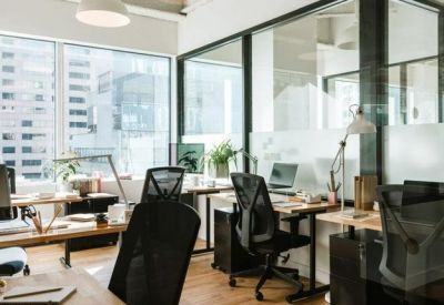 Bright open-plan workspace with multiple desks and city views through large windows.