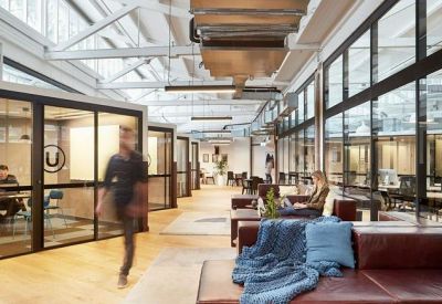 Bright coworking space featuring glass-walled private booths and wooden floors.