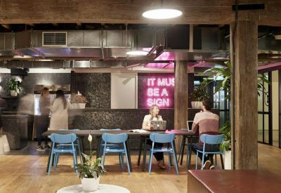 Breakout area with a long table, blue chairs, and a pink neon sign.