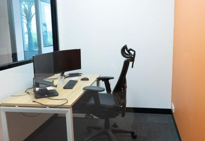 Private office with a light wood desk, ergonomic chair, and an orange feature wall.