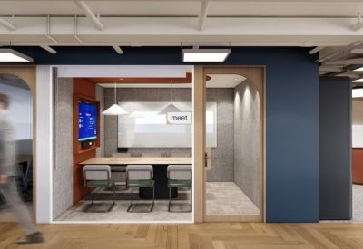 Bright glass-walled meeting room with a wooden table, grey chairs, and orange accent walls.