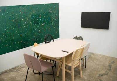 Modern meeting room featuring a light wood table, mixed chairs, and a large green art piece.