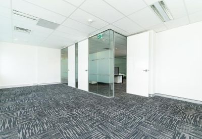 Bright empty office suite with glass partitioning and grey patterned carpet.