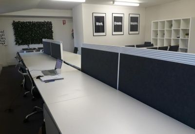 Open-plan coworking area with white desks, privacy screens, and framed wall art.