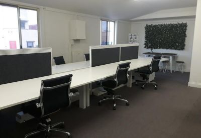 Row of workstations with ergonomic black chairs and a decorative green wall.