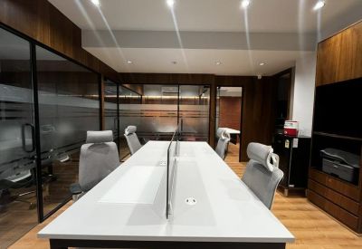 Open-plan workspace with a long central white desk and glass-partitioned perimeter offices.