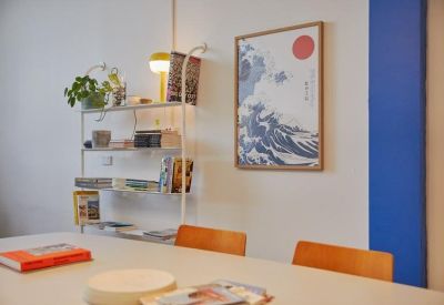 Communal dining area with a long table, orange chairs, and a colorful wall print.