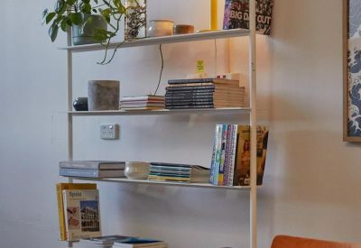 White minimalist shelving unit decorated with books, plants, and a yellow lamp.