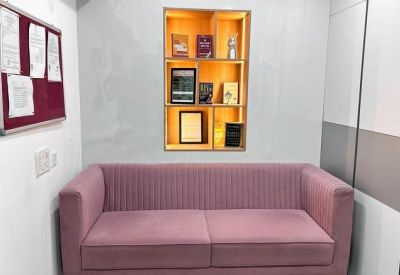 Waiting area with a plush pink sofa and an illuminated wall niche displaying books and awards.