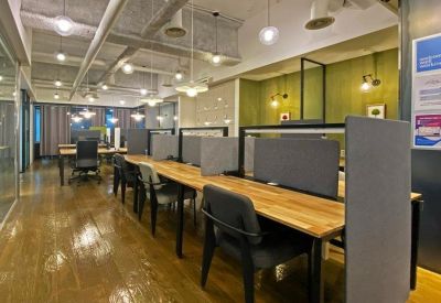 Shared coworking space with long wooden tables, individual partitions, and industrial lighting.