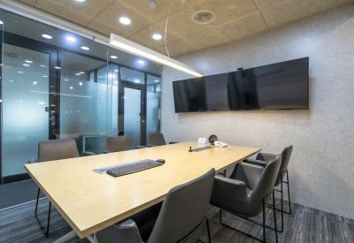 Bright conference room with a light wood table, black chairs, and large wall-mounted screen.