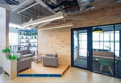 Communal lounge area with grey sofas and a wooden feature wall next to a glass office.
