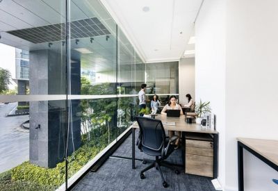 Shared office space featuring a long desk along a floor-to-ceiling glass wall with greenery outside.