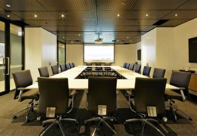 Grand boardroom with a long white table, black executive chairs, and integrated presentation screen.