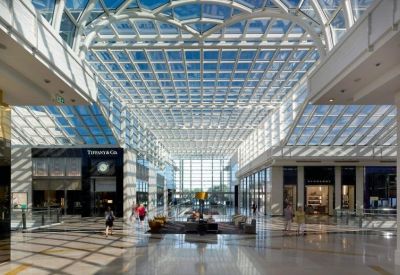 Wide view of a bright retail atrium with a dramatic glass and steel roof.