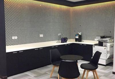 Modern breakroom area with a coffee station, patterned backsplash, and small dining table.