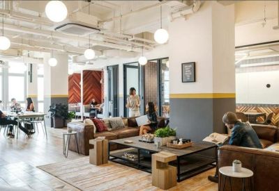 Bright open-plan coworking space with leather sofas, wooden coffee tables, and industrial ceilings.