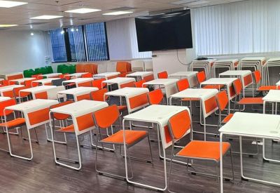 Spacious training room with rows of white desks and bright orange chairs under recessed lighting.