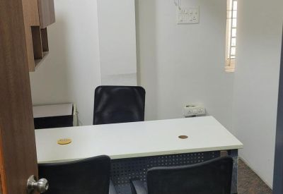 Small private meeting room with a white desk, two black chairs, and a wall-mounted fan.