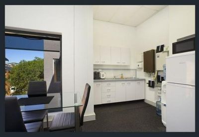 Bright office kitchen and breakroom with white cabinetry and large window views.