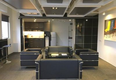 Modern lounge area with black leather seating and a view into a kitchenette area with dark cabinetry.