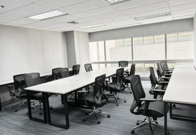 Long white meeting table surrounded by black ergonomic chairs in a brightly lit room.